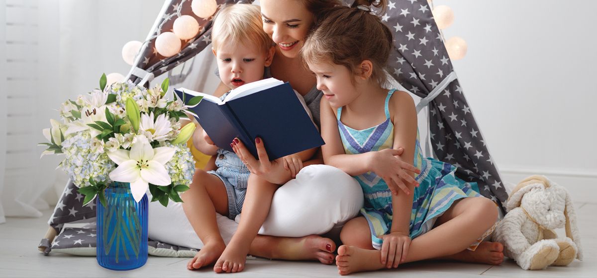 Child reading book with another child and mom watching.